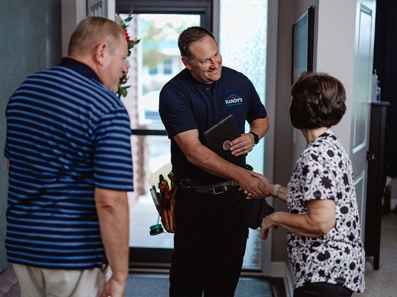 Person greeting a man with a tool belt and clipboard at an entrance.